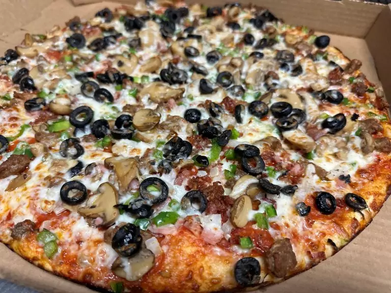 Double Take Pizza mouthwatering four-meat pizza with sliced sausage, pepperoni, peppers, and olives, all covered in melted cheese.